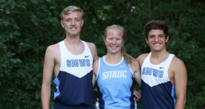 Two male and one female cross country students stand together smiling.